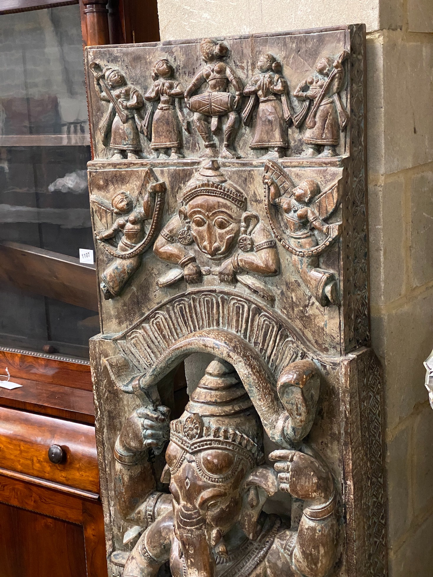 An Indian stained and carved hardwood panel centred with Ganesh, width 54cm, height 160cm